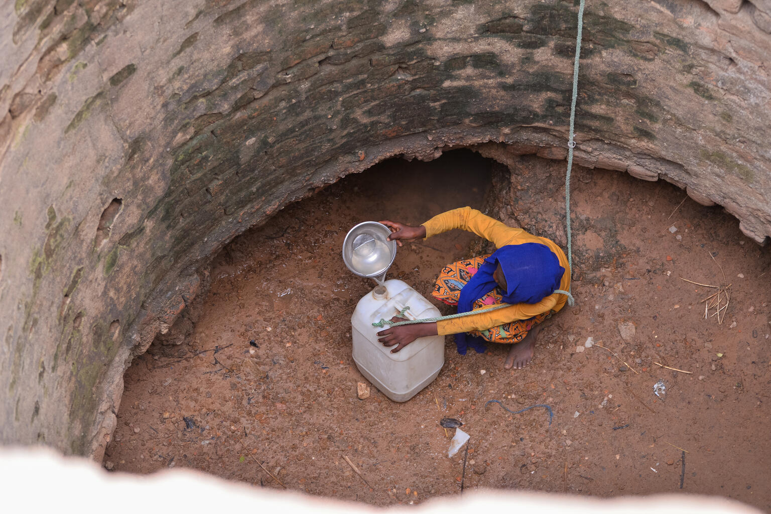 深い井戸の底で、タンクがいっぱいになるまで容器で湧き水をすくって移すムズダリファ（スーダン、2024年5月15日撮影）