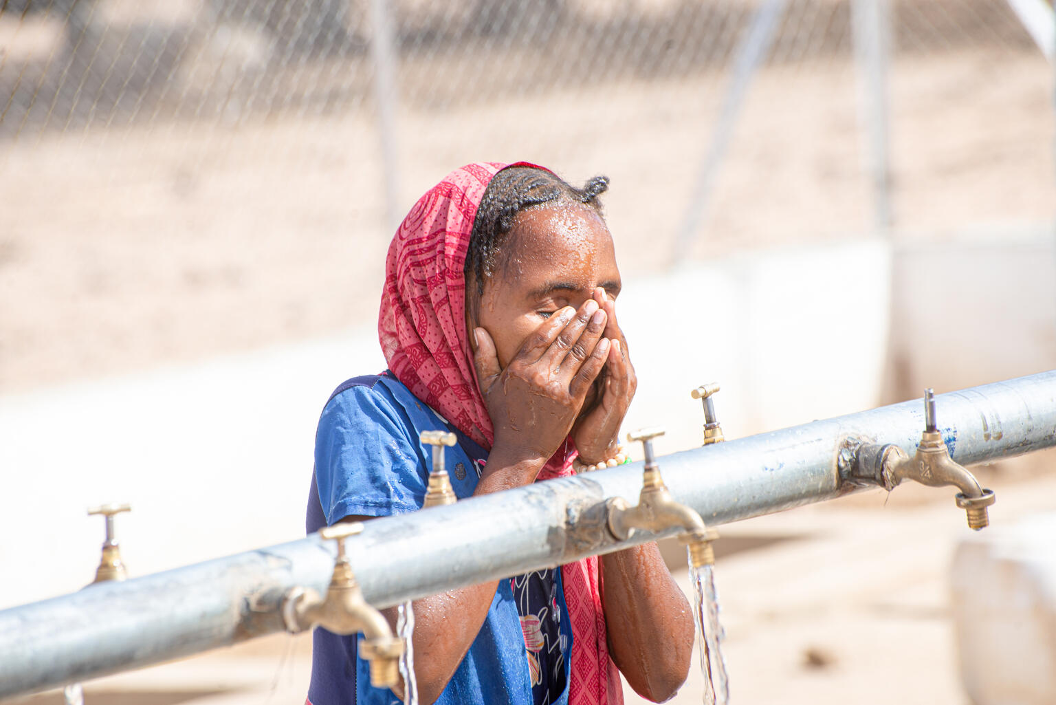 給水施設の蛇口から出てくるきれいな水で顔を洗うヌジュド（スーダン、2024年5月2日撮影）