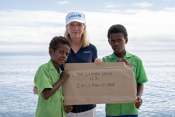 「気候危機は子どもの権利の危機」と書いたボードを手に持つ子どもたちとユニセフ事務局長のキャサリン・ラッセル。(バヌアツ、2024年7月16日撮影) 