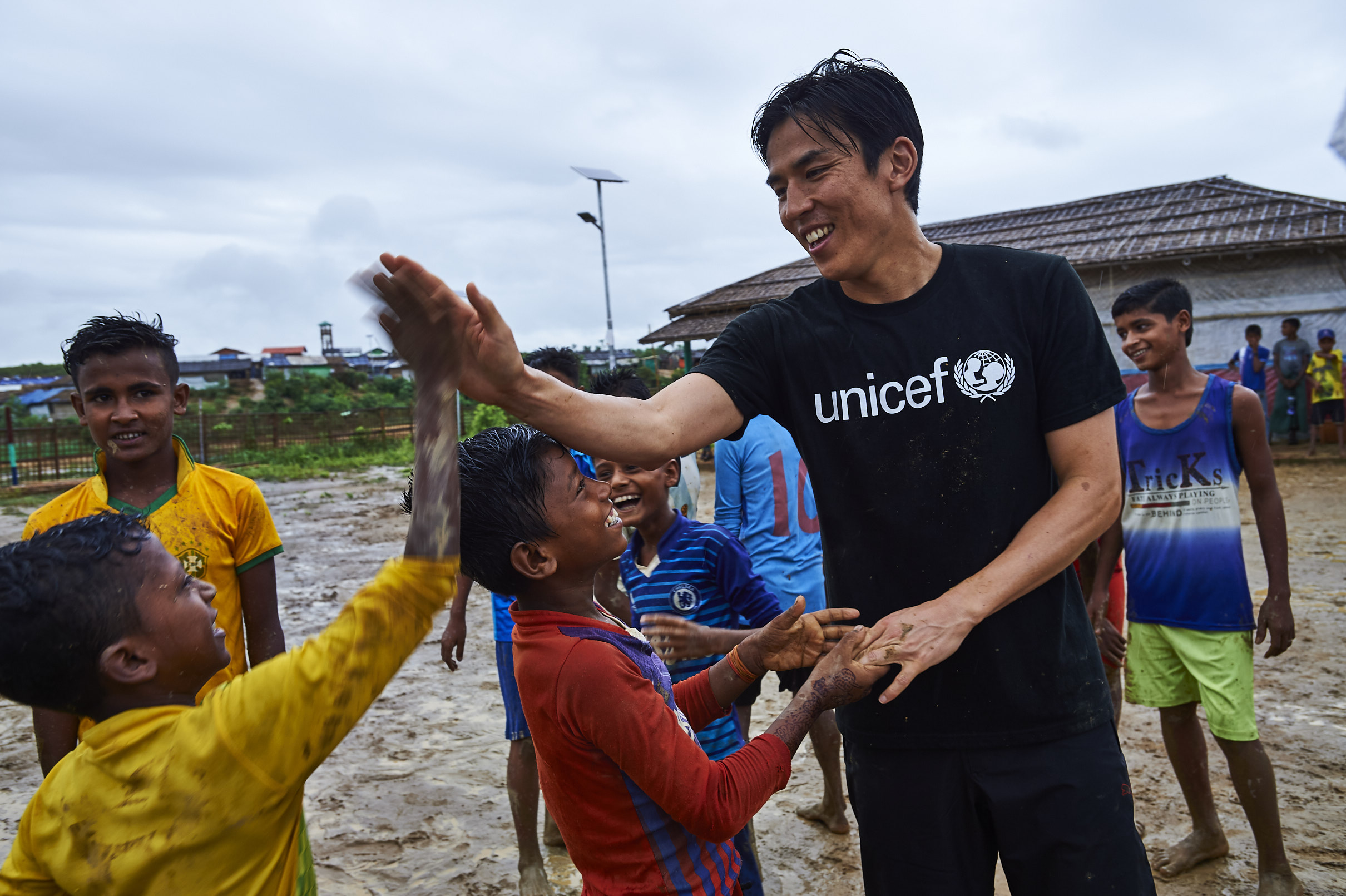 2019年6月6日、バングラデシュ・コックスバザールにあるロヒンギャ難民キャンプで、雨の中子どもたちとボールを追いかけ、笑顔でハイタッチを交わす長谷部大使。