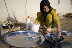 テントの外で食器を洗う13歳の女の子。シリアからヨルダンに避難しているが、避難後は学校に通えていない。