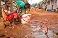 道路にひかれた水道管から流れてくる水を集めるシエラレオネの子どもたち。